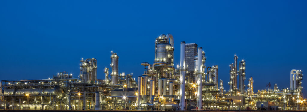 A panoramic view of a modern, illuminated petrochemical plant visible at dusk. Lights from the buildings and streets glow. Several chimneys and distillation towers can be seen. This image was taken with the new Canon EOS 5Ds, long exposure with tripod, industrial district near Rotterdam, Netherlands, Benelux, Europe.
